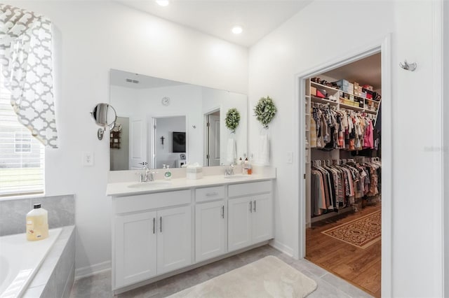 bathroom featuring double vanity, a spacious closet, a relaxing tiled tub, tile patterned flooring, and baseboards