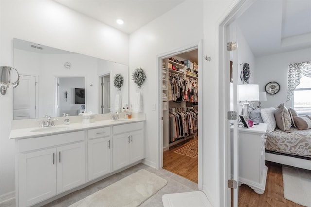 ensuite bathroom with double vanity, a walk in closet, and wood finished floors