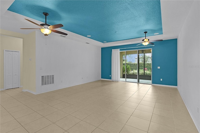 2424 Plumadore Dr, Grand Island, FL 32735 - empty room with a tray ceiling, a ceiling fan, a textured ceiling, baseboards, and light tile patterned floors