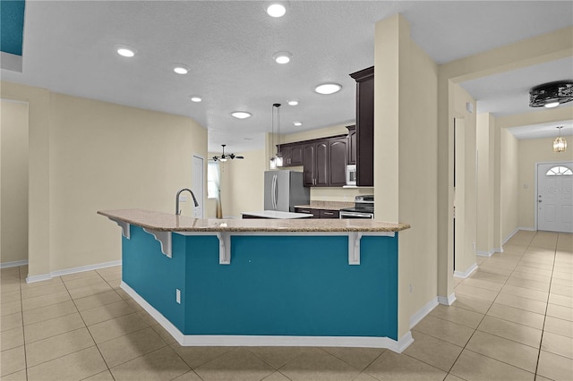 2424 Plumadore Dr, Grand Island, FL 32735 - kitchen featuring stainless steel appliances, a kitchen bar, dark brown cabinets, light tile patterned flooring, and light stone counters