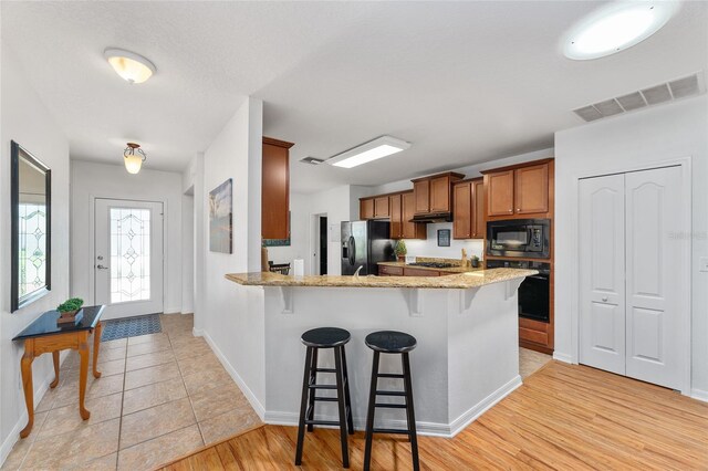 26822 Bull Run, Leesburg, FL 34748 - kitchen with black appliances, brown cabinets, a breakfast bar, light stone countertops, and a peninsula