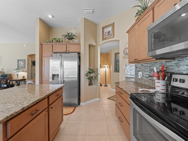2998 Kramer Ct, The Villages, FL 32163 - kitchen featuring stainless steel appliances, arched walkways, backsplash, light tile patterned floors, and light stone counters