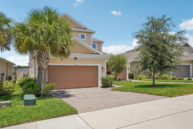 view of front of house with a front yard, driveway, a garage, stucco siding, and central air condition unit