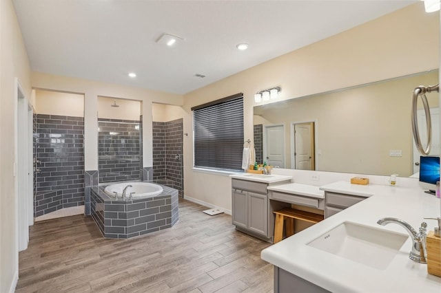 full bath featuring a garden tub, wood finished floors, walk in shower, two vanities, and recessed lighting