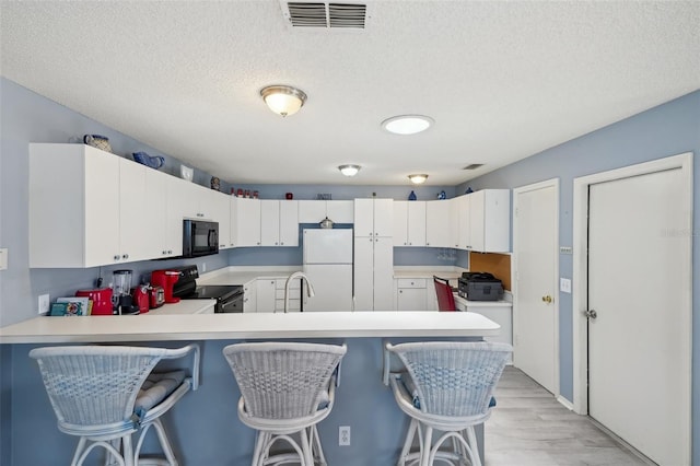 1728 Morelos Rd, The Villages, FL 32159 - kitchen featuring black appliances, light countertops, a peninsula, a textured ceiling, and light wood-style flooring