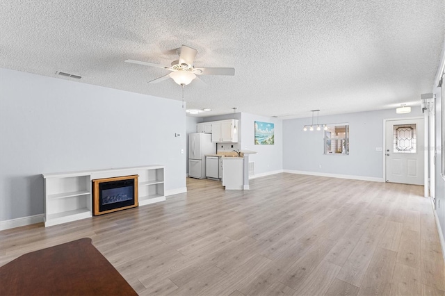 1615 Navidad St, The Villages, FL 32162 - unfurnished living room featuring a textured ceiling, light wood finished floors, ceiling fan, baseboards, and a glass covered fireplace