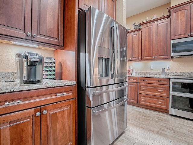 10994 SE 168th Loop, Summerfield, FL 34491 - kitchen with appliances with stainless steel finishes, light stone counters, light wood-style floors, a textured wall, and brown cabinets