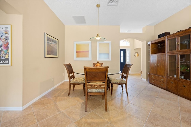 dining area featuring arched walkways, light tile patterned flooring, baseboards, and a textured ceiling