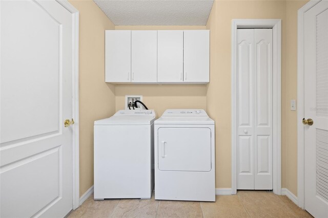 laundry area with separate washer and dryer, cabinet space, baseboards, light tile patterned flooring, and a textured ceiling