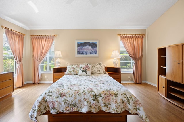 bedroom with light wood-style flooring, baseboards, ceiling fan, and a textured ceiling