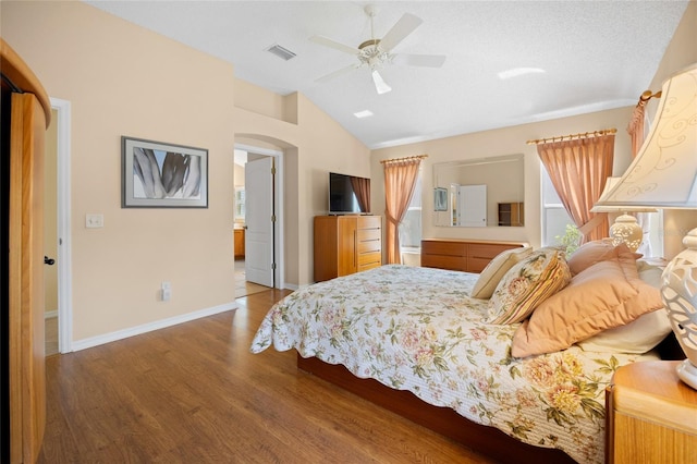 bedroom with wood finished floors, vaulted ceiling, multiple windows, arched walkways, and baseboards