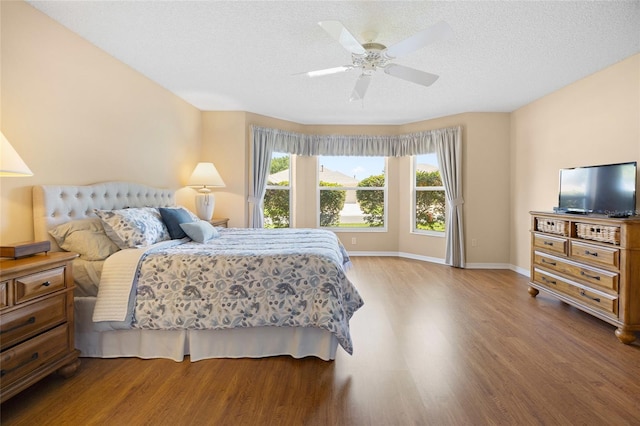 bedroom with wood finished floors, a textured ceiling, baseboards, and a ceiling fan
