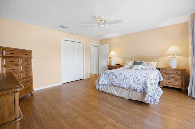 bedroom featuring wood finished floors, multiple closets, baseboards, a ceiling fan, and a textured ceiling