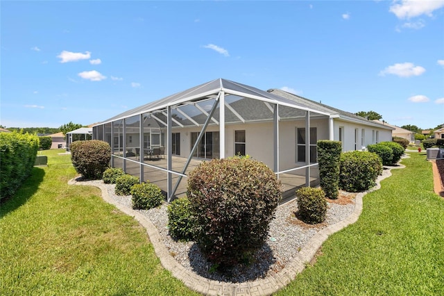 back of house featuring a lawn, stucco siding, a patio, and glass enclosure