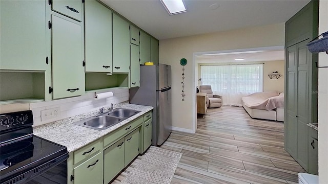 kitchen with black range with electric stovetop, a sink, freestanding refrigerator, and green cabinetry