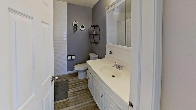 bathroom with vanity, wood finished floors, toilet, a shower with curtain, and baseboards