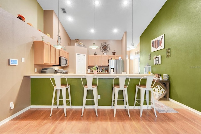 1311 Rain Forest Ln, Minneola, FL 34715 - kitchen with stainless steel appliances, light brown cabinetry, light wood-type flooring, a peninsula, and a kitchen breakfast bar