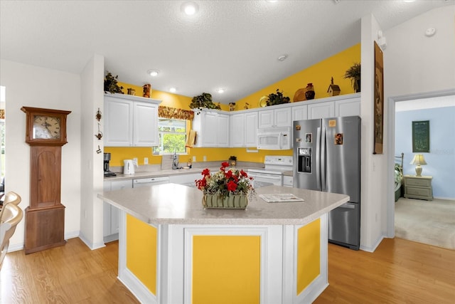 kitchen with white appliances, white cabinets, light wood-type flooring, light countertops, and lofted ceiling