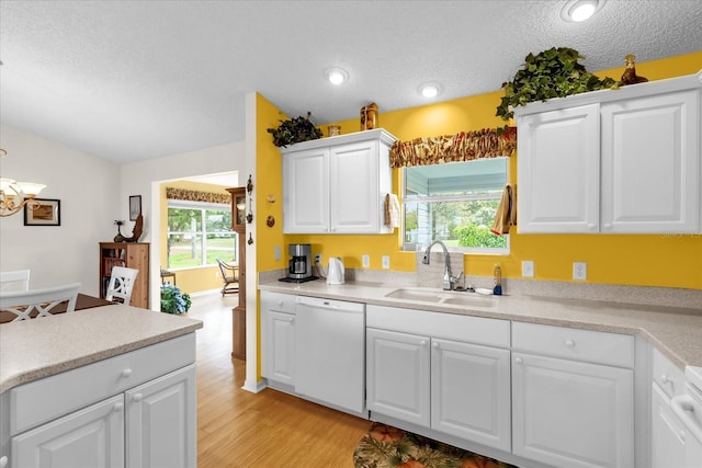 kitchen featuring white dishwasher, a sink, a textured ceiling, light wood finished floors, and white cabinets