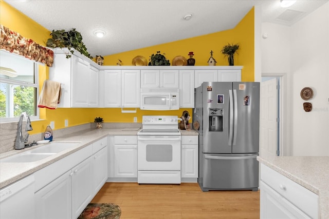 kitchen featuring white appliances, a sink, white cabinets, light wood-type flooring, and vaulted ceiling