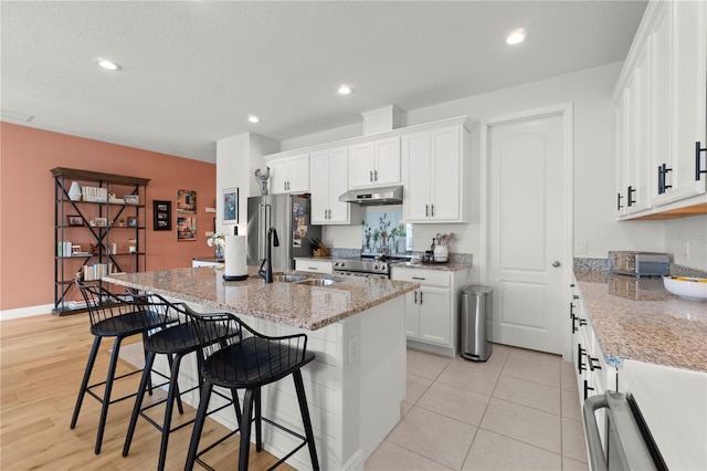 2928 Marlberry Ln, Clermont, FL 34714 - kitchen with under cabinet range hood, a breakfast bar, appliances with stainless steel finishes, white cabinetry, and an island with sink