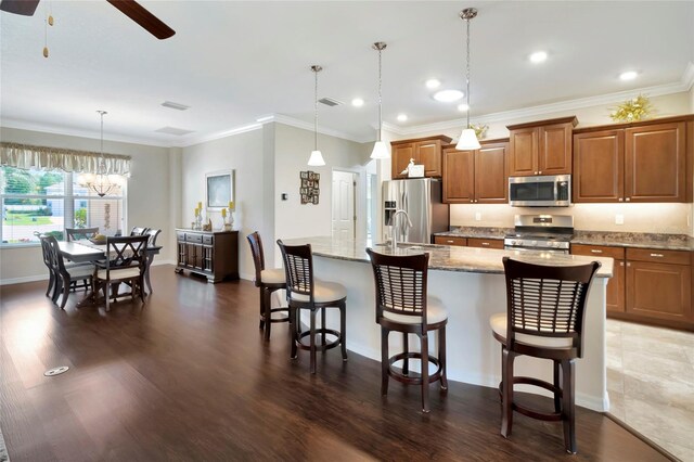 4716 Heritage Trl, Leesburg, FL 34748 - kitchen featuring appliances with stainless steel finishes, brown cabinetry, a ceiling fan, a kitchen bar, and a center island with sink