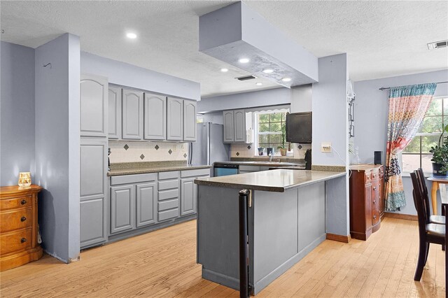 5581 SW 197th Ter, Dunnellon, FL 34431 - kitchen featuring gray cabinetry, a peninsula, light wood finished floors, freestanding refrigerator, and tasteful backsplash