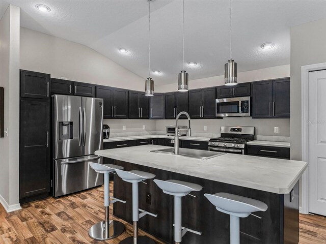 6301 Whittle Ct, The Villages, FL 32163 - kitchen featuring stainless steel appliances, light wood-style flooring, dark cabinetry, a kitchen breakfast bar, and a sink