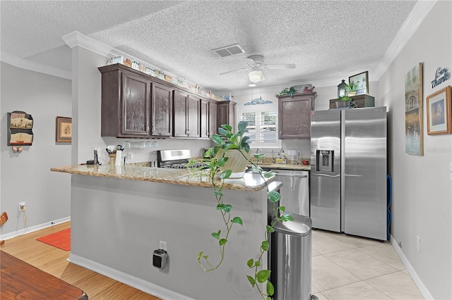 2785 Privada Dr, The Villages, FL 32162 - kitchen with appliances with stainless steel finishes, dark brown cabinets, ornamental molding, ceiling fan, and a peninsula