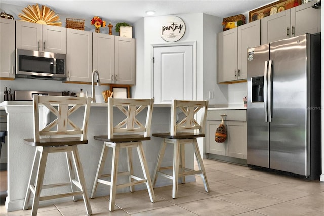 33960 Sky Blossom Cir, Leesburg, FL 34788 - kitchen with stainless steel appliances, light tile patterned floors, a breakfast bar, gray cabinets, and light countertops