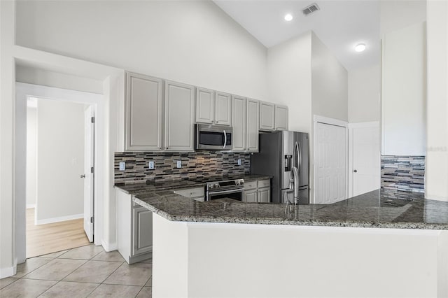 12838 Owasso Ln, Clermont, FL 34711 - kitchen with appliances with stainless steel finishes, light tile patterned flooring, dark stone countertops, decorative backsplash, and a peninsula