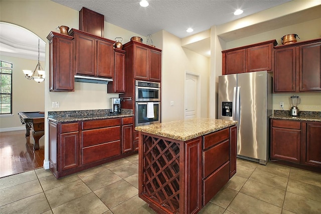 21206 Canoe Pass St, Clermont, FL 34715 - kitchen featuring appliances with stainless steel finishes, reddish brown cabinets, dark stone countertops, a kitchen island, and a textured ceiling