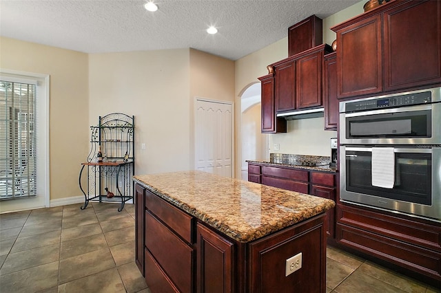21206 Canoe Pass St, Clermont, FL 34715 - kitchen with dark brown cabinets, double oven, a center island, arched walkways, and a textured ceiling