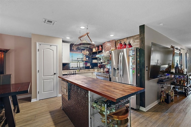 12952 Del Lago Dr, Astatula, FL 34705 - kitchen featuring wood counters, white cabinets, light wood-style flooring, a textured ceiling, and appliances with stainless steel finishes