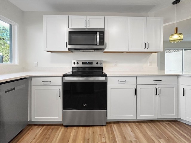 5136 Cedar Hammock Dr, Sarasota, FL 34232 - kitchen with stainless steel appliances, white cabinets, light wood-type flooring, light countertops, and hanging light fixtures