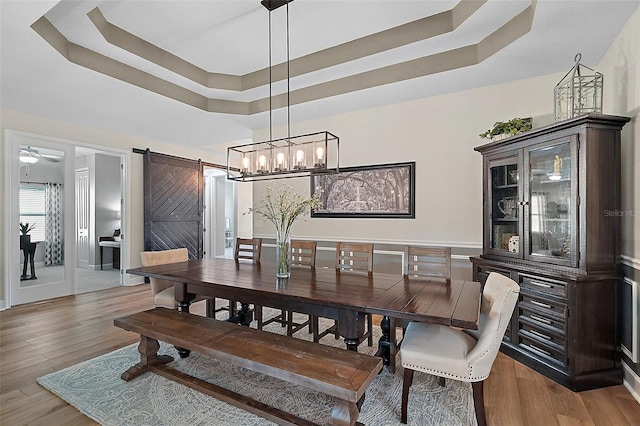 440 Bellissimo Pl, Howey In The Hills, FL 34737 - dining area featuring a barn door, a tray ceiling, light wood-type flooring, and a ceiling fan