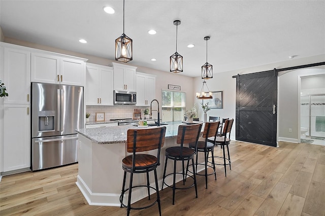 440 Bellissimo Pl, Howey In The Hills, FL 34737 - kitchen featuring stainless steel appliances, a barn door, light wood-type flooring, white cabinetry, and a kitchen island with sink