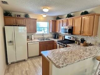 3337 Candlebrook St, The Villages, FL 32162 - kitchen featuring stainless steel appliances, a sink, a peninsula, light wood-style flooring, and a textured ceiling
