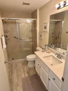 3337 Candlebrook St, The Villages, FL 32162 - bathroom featuring a textured ceiling, toilet, vanity, a shower stall, and wood finished floors