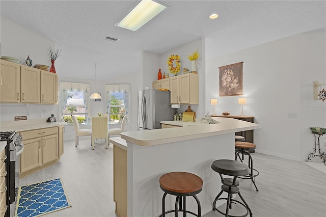 2738 Morven Park Way, The Villages, FL 32162 - kitchen featuring stainless steel appliances, a kitchen breakfast bar, a textured ceiling, light wood-style floors, and light brown cabinetry