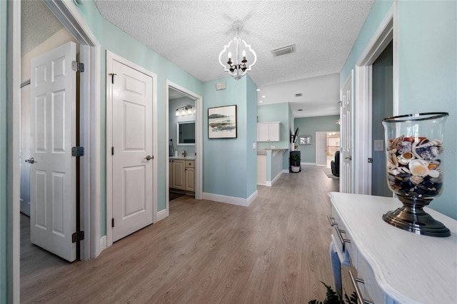 9430 SE 176th Saffold St, The Villages, FL 32162 - hallway featuring a chandelier, light wood-style flooring, a textured ceiling, and baseboards
