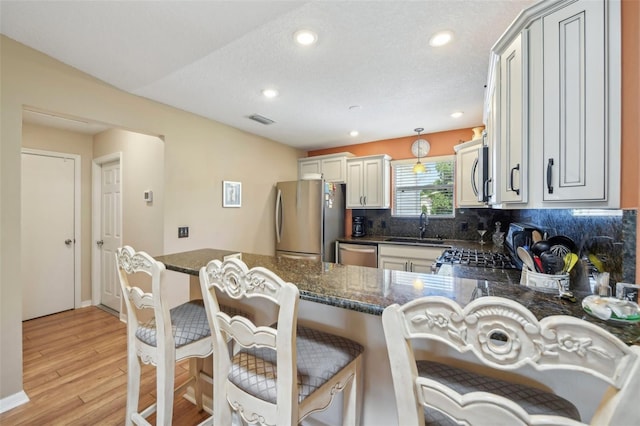 8039 SE 174th Belhaven Loop, The Villages, FL 32162 - kitchen featuring appliances with stainless steel finishes, a sink, tasteful backsplash, light wood finished floors, and a peninsula