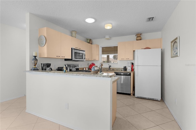 9321 SE 172nd Augusta Ln, The Villages, FL 32162 - kitchen featuring appliances with stainless steel finishes, light brown cabinetry, a peninsula, a textured ceiling, and light tile patterned floors