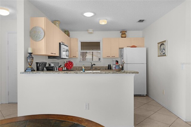 9321 SE 172nd Augusta Ln, The Villages, FL 32162 - kitchen featuring freestanding refrigerator, a peninsula, light tile patterned floors, light brown cabinetry, and a textured ceiling