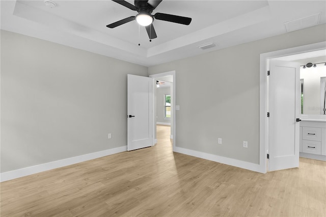 1115 W Geneva Pl, Citrus Springs, FL 34434 - unfurnished bedroom featuring a tray ceiling, light wood-style flooring, baseboards, ceiling fan, and ensuite bathroom