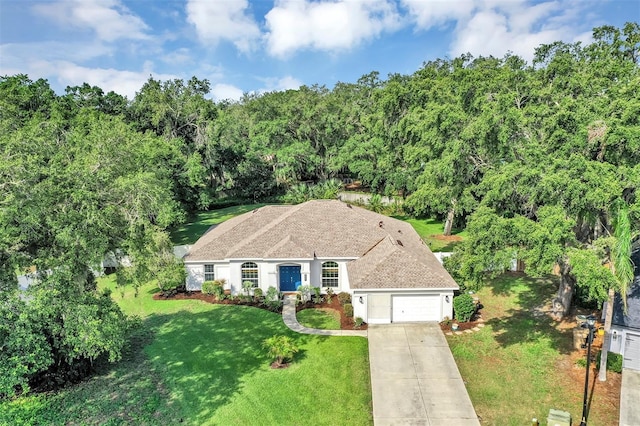 34231 Shadewood Cir, Leesburg, FL 34788 - view of front of home featuring an attached garage, a front lawn, concrete driveway, a shingled roof, and stucco siding