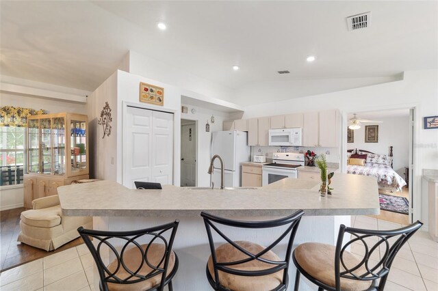 8850 SE 156th St, Summerfield, FL 34491 - kitchen with white appliances, a breakfast bar, vaulted ceiling, light countertops, and light tile patterned floors