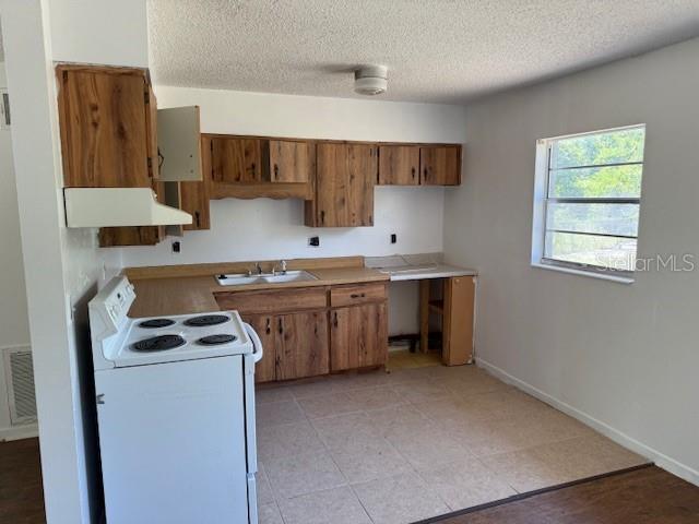 1109 Willow Ct, Tavares, FL 32778 - kitchen with white range with electric cooktop, custom range hood, brown cabinets, a sink, and a textured ceiling
