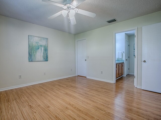 2799 Privada Dr, The Villages, FL 32162 - unfurnished bedroom featuring light wood-style flooring, a textured ceiling, ensuite bathroom, and a ceiling fan