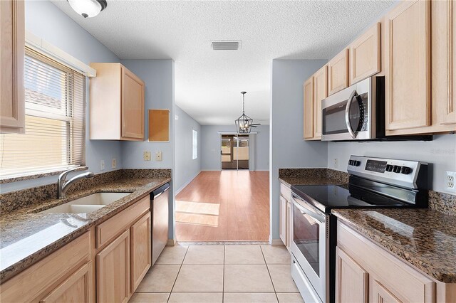 1116 San Bernardo Rd, The Villages, FL 32162 - kitchen with stainless steel appliances, light brown cabinetry, a sink, plenty of natural light, and a textured ceiling